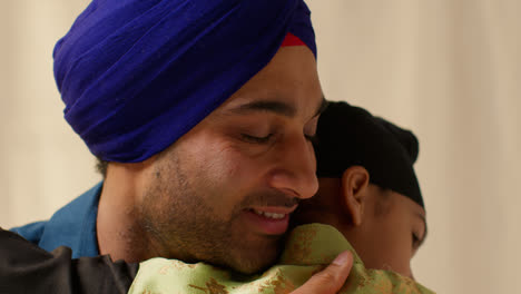 Close-Up-Studio-Shot-Of-Sikh-Father-Embracing-Son-Both-Wearing-Turbans-Against-Plain-Background-4